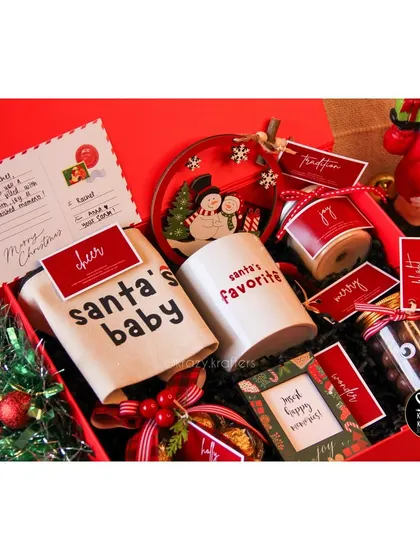 Our 'Holiday Home' Christmas hamper is an experience in a box, filled with a 'Santa's Favorite' mug, a snowman-themed plate, a 'Santa's Baby' pouch, and other festive delights.