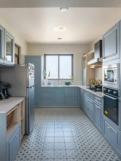 This galley kitchen in a calming dusty blue is both charming and practical. The patterned floor tiles and glass-front cabinets add a touch of classic style to the modern shaker-style doors.