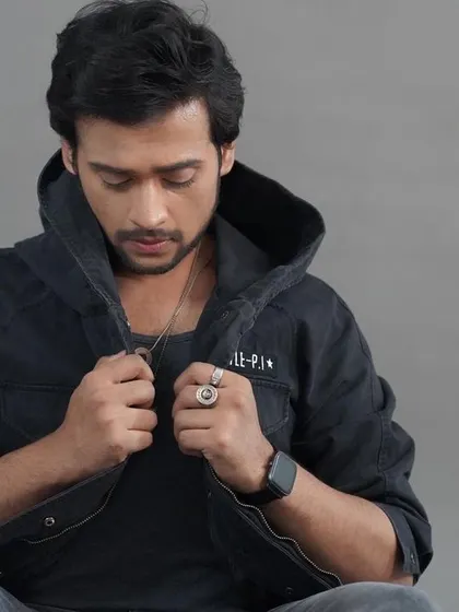 A thoughtful, seated studio portrait. The model adjusting his jacket creates a natural, candid feel within a controlled studio environment.