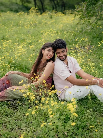 A full view of the couple sitting back-to-back, surrounded by nature. It's a classic pre-wedding pose that feels relaxed and comfortable.