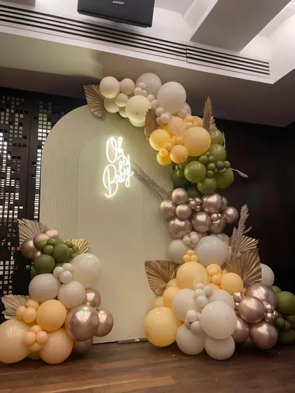 An elegant baby shower setup featuring an 'Oh Baby' neon sign and a beautiful organic balloon arch in earthy tones of olive green, peach, and metallic rose gold.