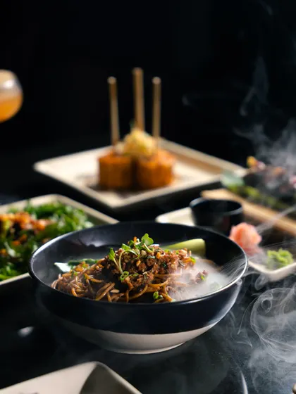 Flavours that touch the soul. A spread of our pan-Asian dishes, including steaming Dan Dan noodles, crispy corn, and fresh greens, ready to be shared.