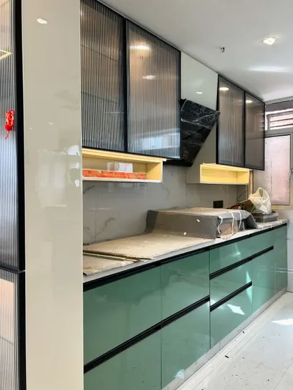 Another angle of the mint green and fluted glass kitchen during installation. You can see the precision of the factory-made modules and the stylish black profile handles.