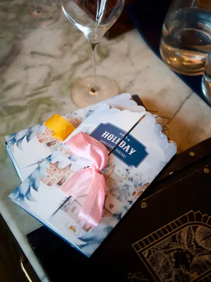Our special Holiday Menu, designed like a Christmas card and tied with a pink ribbon. Every detail is considered to make the experience feel special.