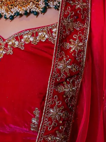This image highlights the intricate floral gold and silver embroidery on the border of the red velvet lehenga, showing the quality of the outfits I offer for rent.