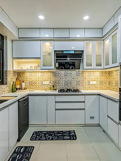 A bright, all-white U-shaped kitchen with integrated appliances and a patterned tile backsplash. The glass-front upper cabinets help to lighten the space.