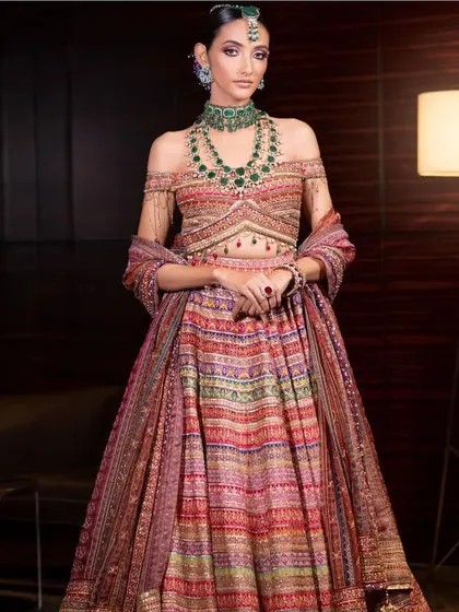 A full-length shot of a modern bride in a multi-colored striped lehenga. This shows the importance of understanding fashion trends to create relevant and contemporary makeup looks.