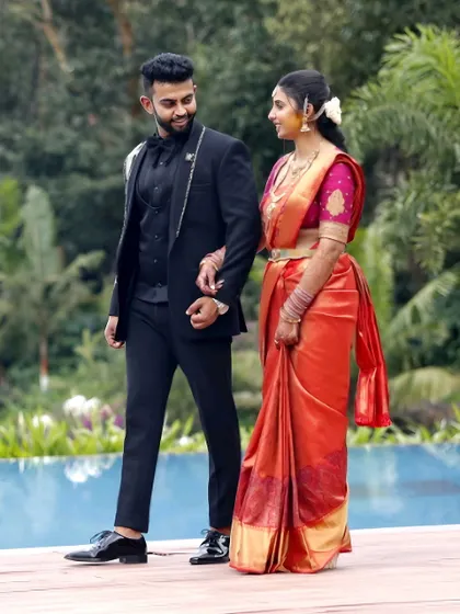 A candid shot of the couple walking together, sharing a happy glance. The groom in a sharp suit and the bride in a vibrant silk saree perfectly blend modern and traditional styles.