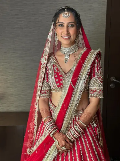 A full portrait of this happy bride. Her classic red lehenga is paired with a minimal glam look, featuring a flawless base and defined eyes, making her look timeless.