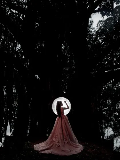 A creative silhouette shot using a ring light, highlighting the beautiful shape of the pink wedding gown against the dark backdrop of a banyan tree.