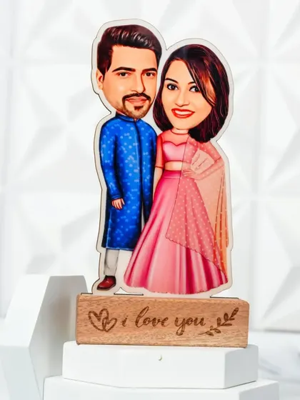 A caricature of a couple in traditional Indian attire, mounted on a wooden stand engraved with "I love you".