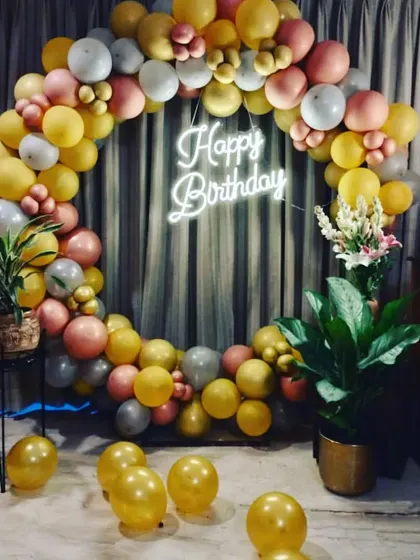An elegant birthday balloon ring set up in a living room. The gold, peach, and white balloons create a warm and inviting photo backdrop, complete with a neon sign.
