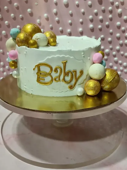A simple and sweet "Baby" cake. The textured white buttercream is adorned with a cascade of pastel and gold chocolate spheres.
