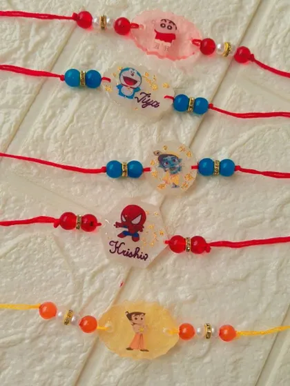 A set of cute, cartoon-themed resin rakhis for kids, featuring characters like Shinchan, Doraemon, and Spiderman.