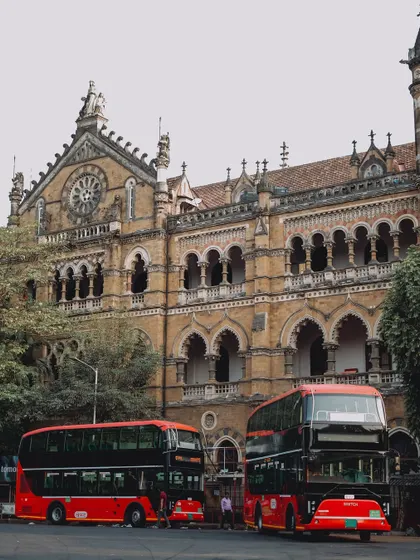 Wide shots of the CSMT building, showcasing its intricate Victorian Gothic design. The presence of the iconic red double-decker buses adds to the vintage charm.