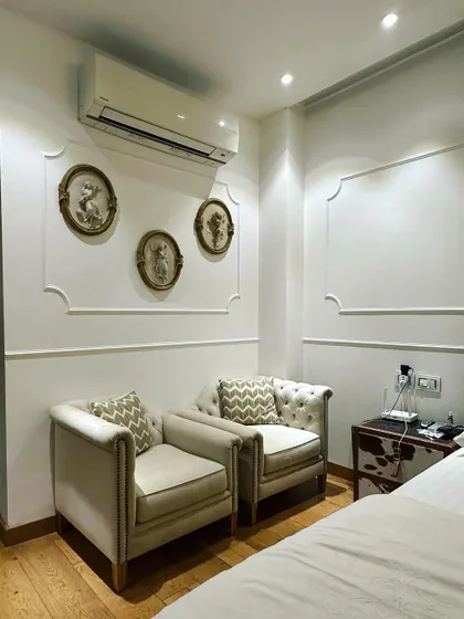 A classic bedroom corner design in a Central Park Resort residence. The tufted armchairs and ornate wall frames create an elegant and timeless seating area.