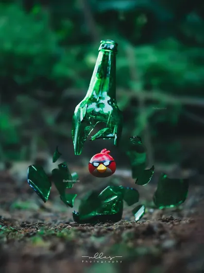 An Angry Birds toy is captured mid-air as if it has just shattered a green glass bottle. This fun and creative shot brings a popular game to life using clever photography techniques.
