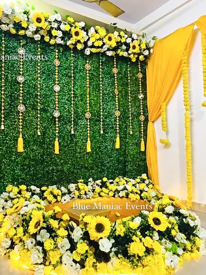 A grand Haldi setup with a green wall, yellow drapes, and a floor seating area surrounded by sunflowers. This design is perfect for making a statement.
