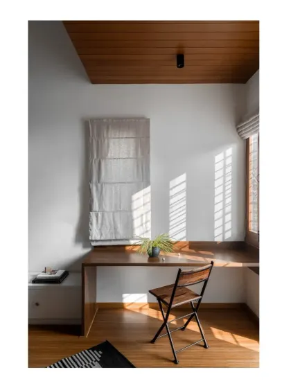 A simple, sunlit study corner in the guest room, where a wooden desk and chair create a functional and peaceful workspace.