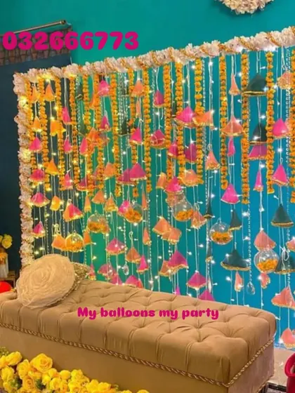 This Mehendi photo booth features a teal backdrop with hanging strings of marigolds, tassels, and fairy lights for a festive and bright look.