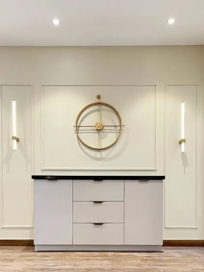 A minimalist crockery unit with a statement wall clock and modern wall sconces. The clean lines and simple geometry make it a sophisticated addition to any dining space.