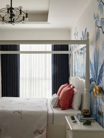 A full view of the boy's bedroom, showing how the vibrant wallpaper wraps around the room. The dark blue curtains frame the window, balancing the brightness of the walls.