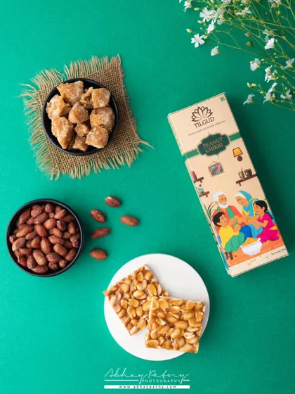 A vibrant, high-contrast flat lay like this one for peanut chikki makes the product jump off the screen. The green background complements the earthy tones of the peanuts and jaggery, creating a visually appealing shot for social media.