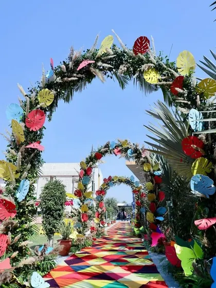 A whimsical and colorful floral entry arch decorated with paper leaves in various hues, perfect for a fun, carnival-themed event.
