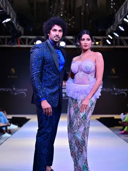A powerful pose from both models, highlighting the blend of modern menswear and elaborate womenswear couture.