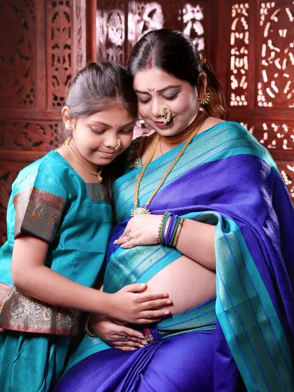 Welcoming a new baby is a family affair. Here, a mother-to-be shares a quiet moment with her daughter, both dressed in beautiful traditional sarees, celebrating their growing family and cultural roots.