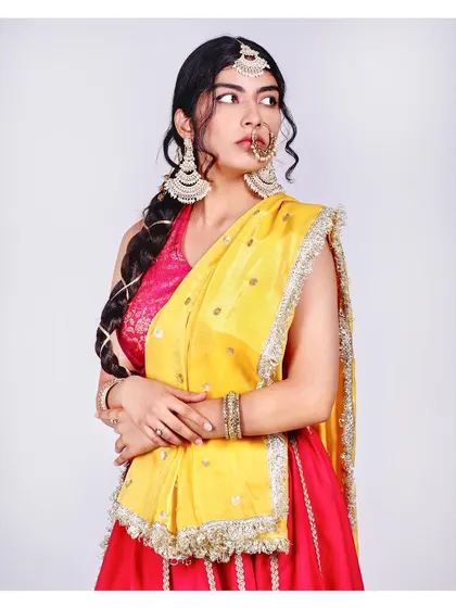 A beautiful three-quarter portrait in a bright pink and yellow lehenga. The braided hairstyle and traditional jewelry complete this classic ethnic look.