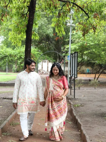 A beautiful outdoor shot of the couple at their baby shower celebration. The mom-to-be is glowing in a traditional saree with soft, elegant makeup.
