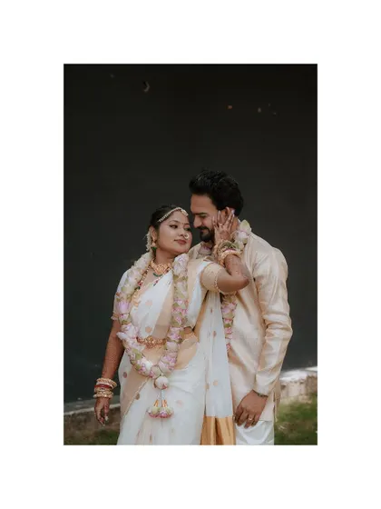 A gentle, loving portrait of the couple against a simple dark background, highlighting their traditional garlands and attire.