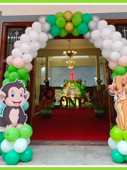 A grand balloon archway welcomes guests to a jungle-themed first birthday. Character cutouts of Simba and a monkey stand at the entrance, setting the stage for the wild adventure inside.