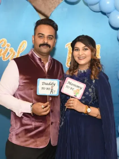 Having fun with props! The "Daddy to be" and "Mommy to be" signs add a playful touch to this baby shower photo against a pink and blue balloon arch.