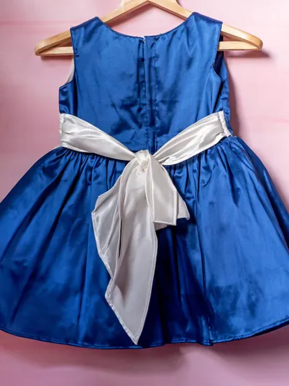 A classic party dress in royal blue satin. This view highlights the beautiful, oversized white sash that ties into a dramatic bow at the back, adding a touch of timeless elegance.