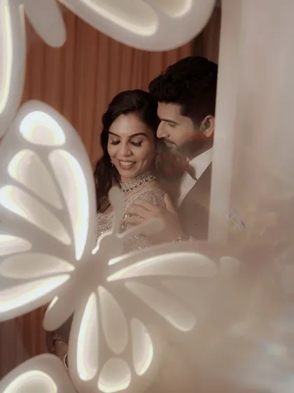 A creative shot of the couple seen through illuminated butterfly decor, creating a dreamy and magical portrait.
