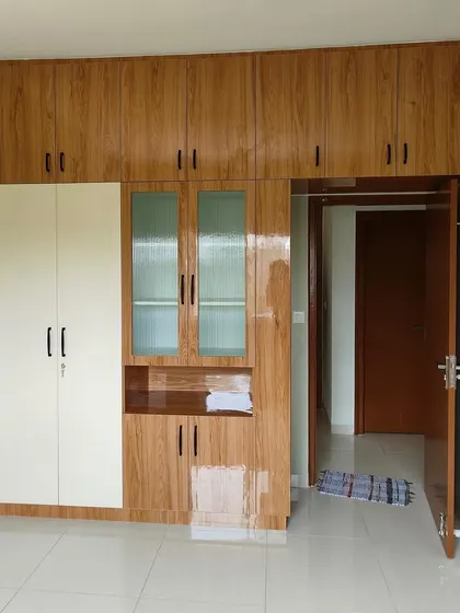 A guest bedroom wardrobe in a warm wood laminate, featuring a glass-fronted display section for books or decor.