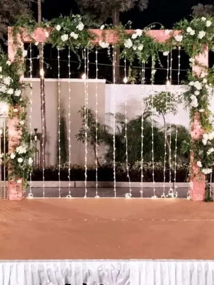 This beautiful wedding arch combines a rustic wooden frame with delicate white florals, lush greenery, and cascading fairy lights. It creates a simple yet enchanting backdrop for an evening ceremony or reception.