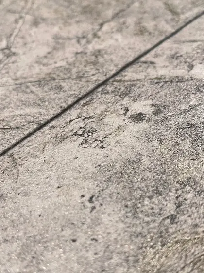 A close-up of a grey stone-textured wallpaper. The subtle cracks and imperfections in the design give it a realistic and organic feel, perfect for adding depth and interest to a minimalist space.