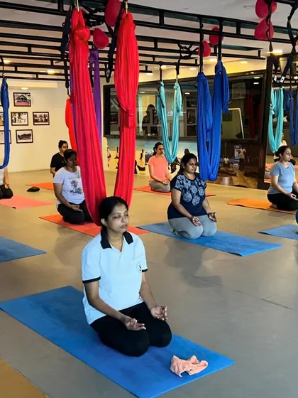 A moment of calm before our aerial yoga class begins. Students are centered in Vajrasana (Thunderbolt Pose) on their mats, with the colorful aerial silks hanging above, ready for practice.