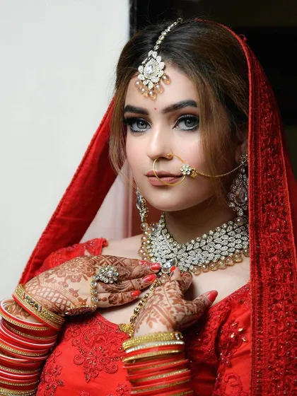 An elegant bridal portrait showcasing the bride's stunning red lehenga and diamond jewelry. Her pose is graceful, highlighting the intricate details of her wedding day look.