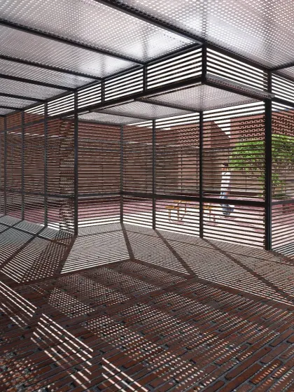 An exploration of light and shadow at Studio Tarai. The slatted steel pergola and wall screens are not just structural; they are designed to catch the sun and cast dynamic geometric patterns across the brick floor, making light a tangible material that changes throughout the day.