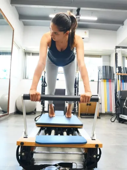 A client demonstrates a powerful move on the reformer. This machine uses spring resistance to lengthen and strengthen muscles simultaneously, helping you redefine your body's limits.