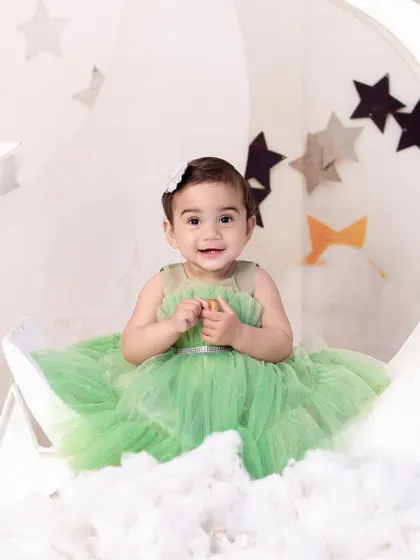 A close-up of the baby girl in the green dress, showing her happy smile and the delicate details of her outfit.