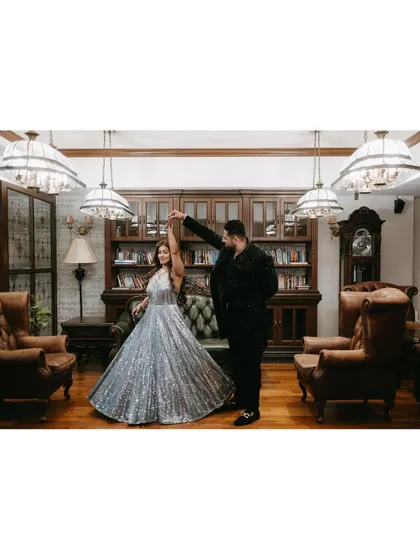 The groom twirls his bride in a beautiful silver gown in a sophisticated library setting, capturing a moment of dance and romance.