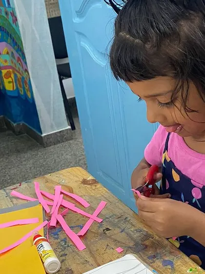 The focus required for cutting is a big step in developing fine motor skills. This little artist is carefully cutting strips of paper for her mosaic project, showing great concentration and determination.
