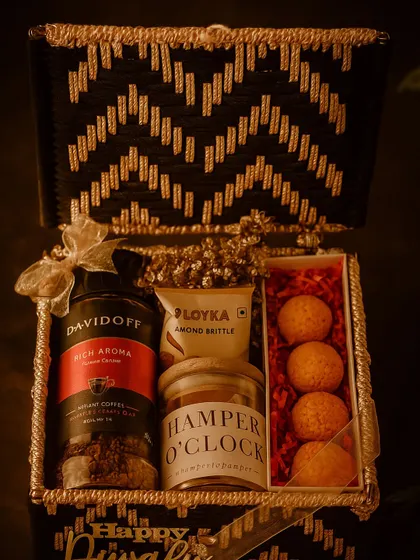 For the coffee connoisseur, this Noir & Gold festive box is pure indulgence. It features rich Davidoff coffee, almond brittle, premium cashews, and unique ladoo-shaped candles, all housed in a striking black and gold handcrafted basket for a truly luxurious feel.