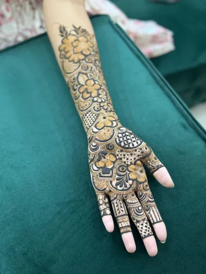 A beautiful full-hand henna design for a bride's sister, featuring a mix of floral patterns and geometric checkers. The design extends up the forearm for a balanced and complete look.