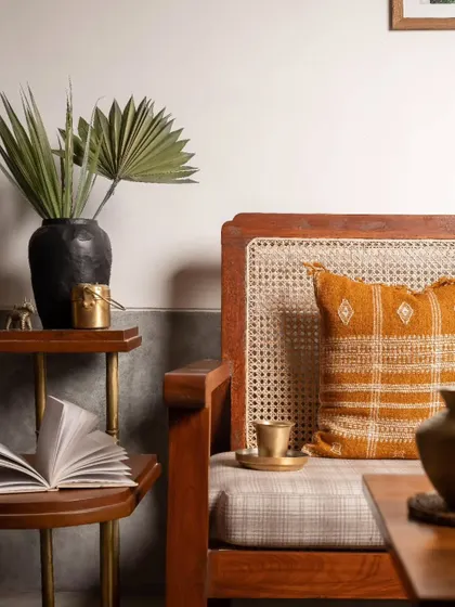 A close-up detail of the custom-designed armchair, showing the combination of teak wood, cane weaving, and brass accents that define the furniture in this home.